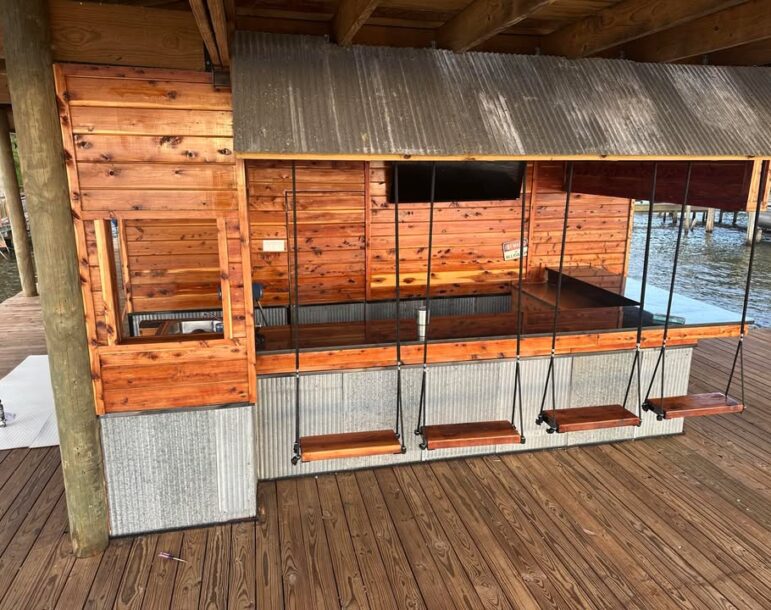 Outdoor dockside bar built with Eastern Red Cedar siding and countertops, featuring unique swing seating and corrugated metal accent