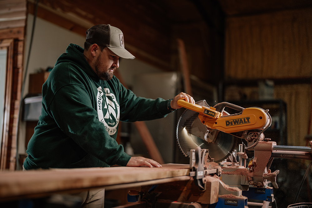 Man operating a Dewalt miter saw in a workshop, focused on cutting lumber, showcasing craftsmanship relevant to Dutch lap siding installation.