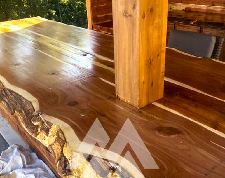 Close-up of a polished live-edge Eastern Red Cedar bar top with natural wood grain and character, supported by a cedar post in an outdoor kitchen structure