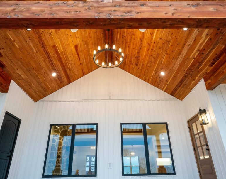 Vaulted porch ceiling finished with Eastern Red Cedar tongue and groove boards, complemented by a rustic chandelier and white vertical siding